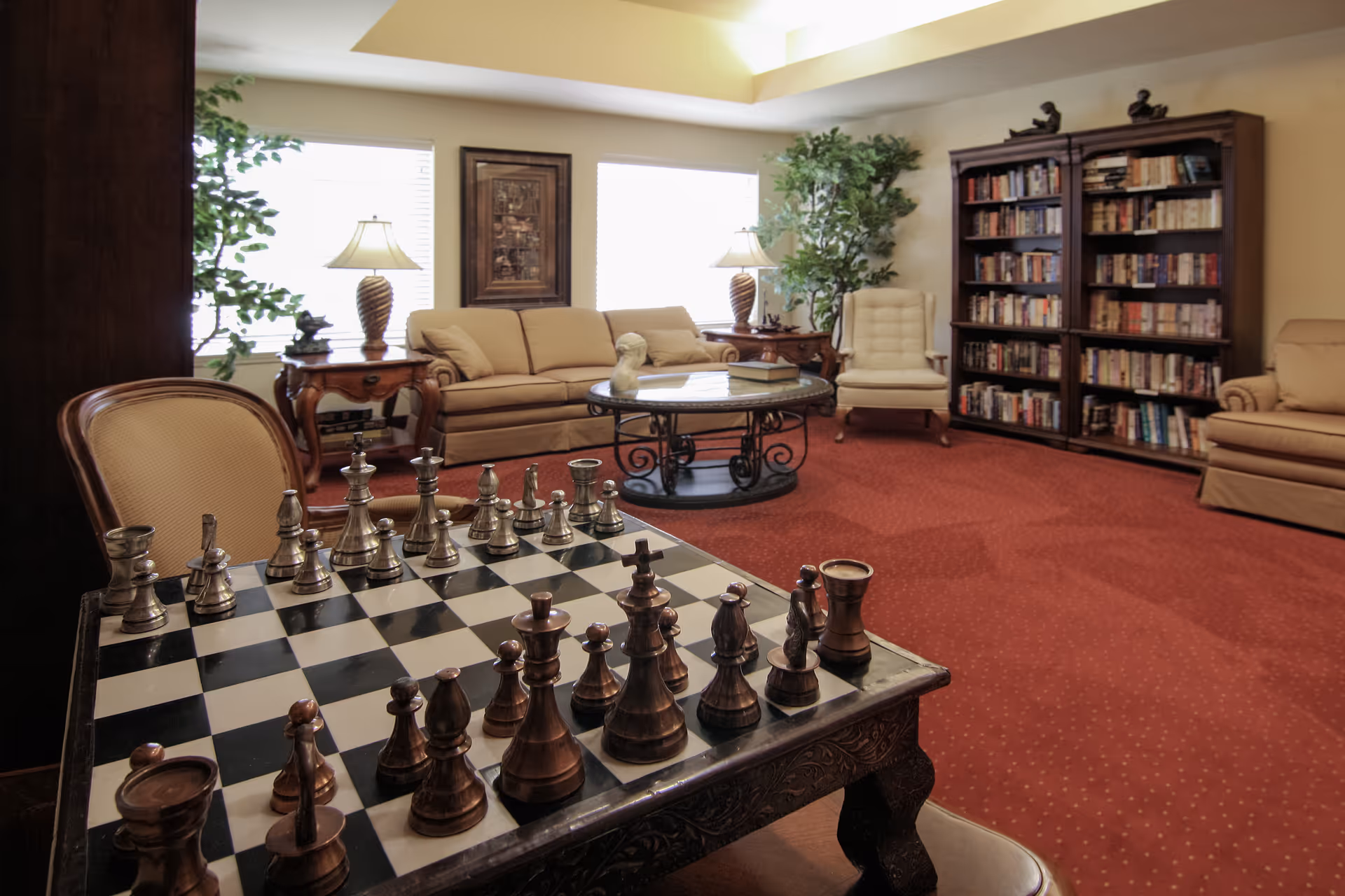 Cozy lounge with a chessboard in the foreground, sofas, lamps, a coffee table, and a bookcase.