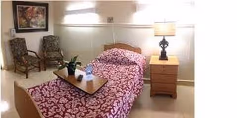 A small bedroom featuring a single bed with a pink-patterned cover, two chairs, and a nightstand.