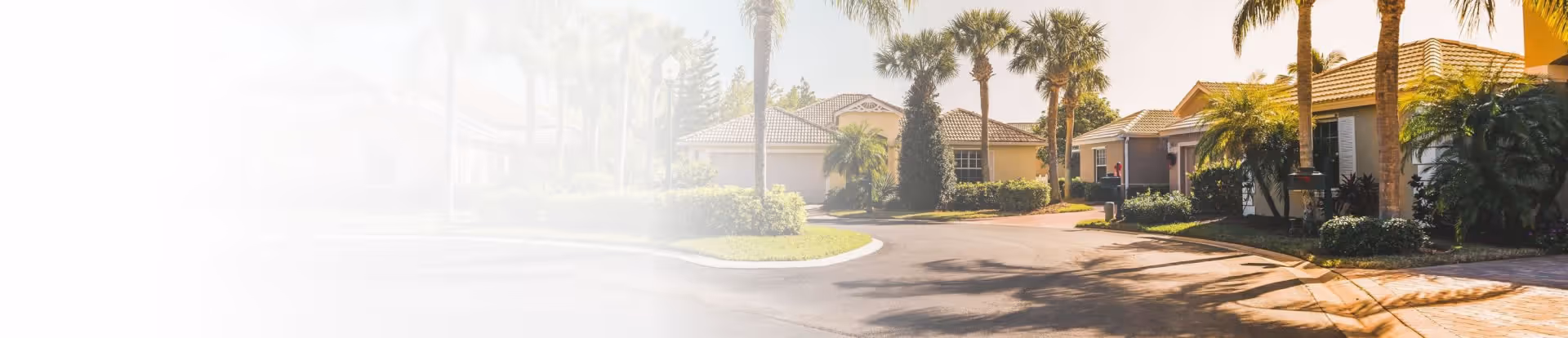 Exterior view of a senior living campus with low-rise beige buildings, palm trees, and a curved driveway.