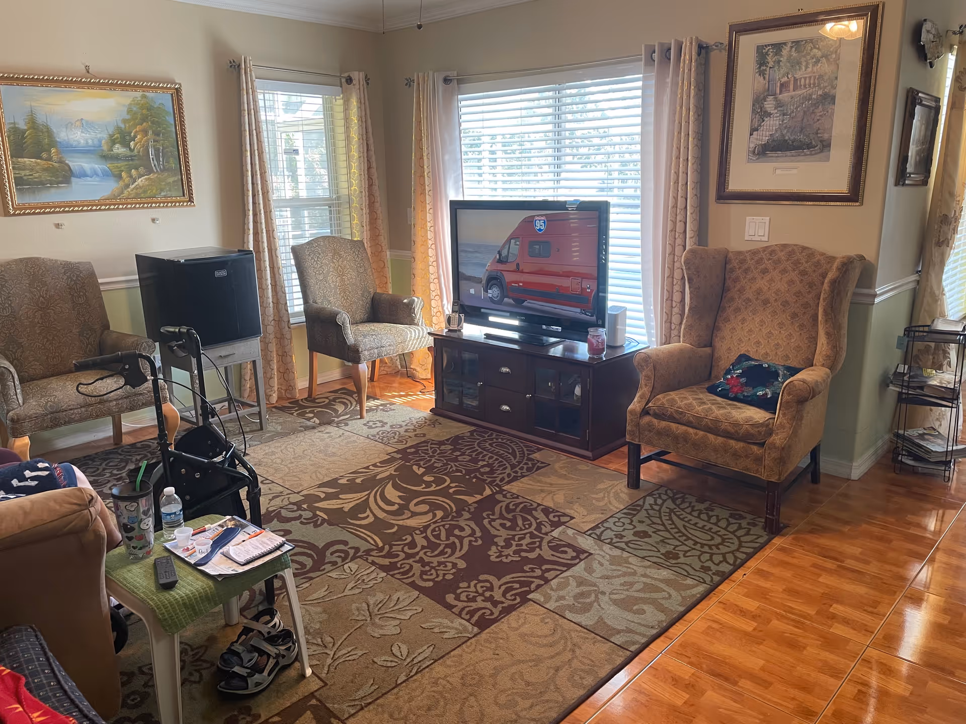 Cozy living room with armchairs, a TV, rug, windows, and a walker in view.