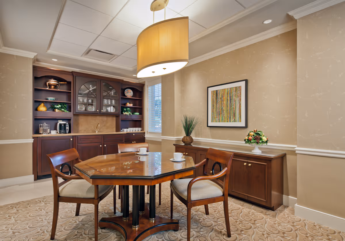 A small elegant dining/meeting room with a wooden table and chairs, built-in cabinets, decorative artwork and a large pendant light.