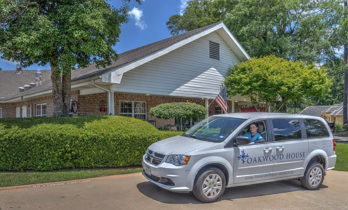 Front exterior of Oakwood House senior living facility with a branded van parked by the entrance and a staff member in the driver's seat.