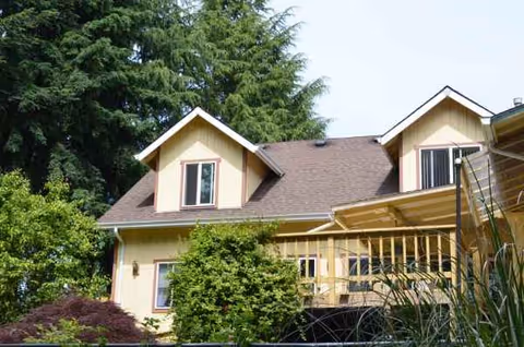 Exterior view of a beige house-like care home with a covered porch and greenery.
