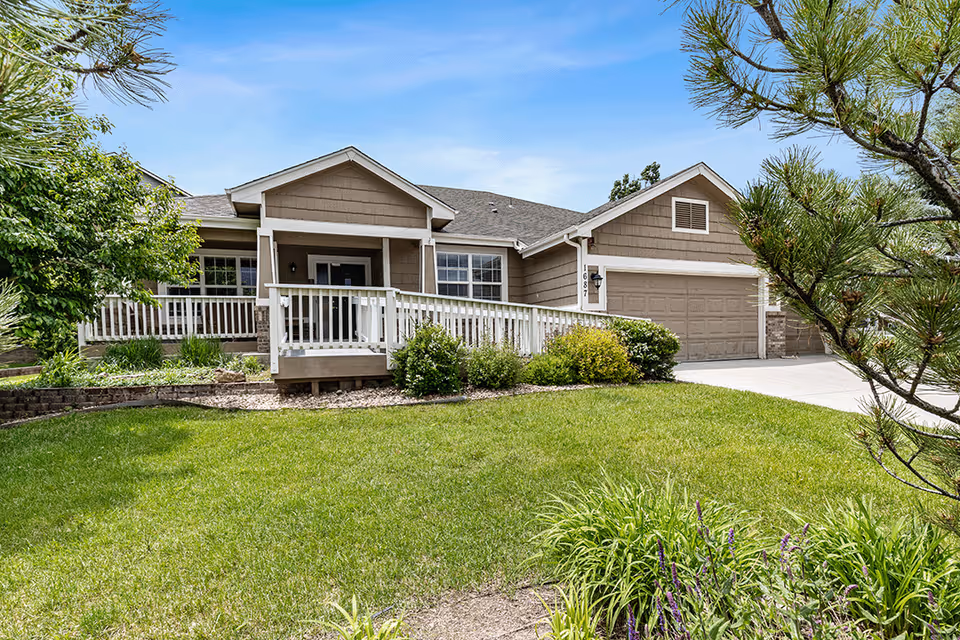 Front exterior of a single-story suburban house with a covered porch and ramp, attached garage, and a landscaped lawn.
