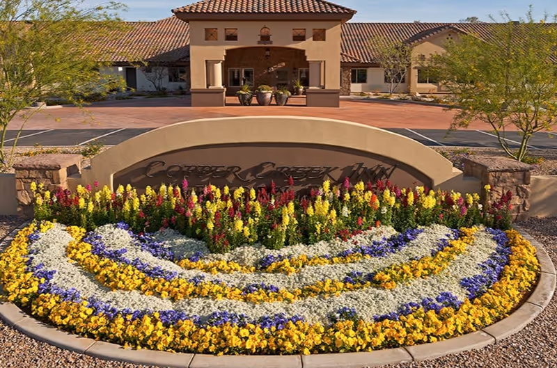 Exterior entrance of Copper Creek Inn with a colorful flower bed and curved sign.