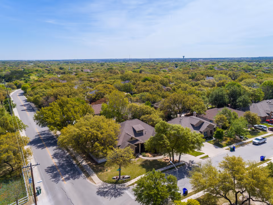 Aerial view of a residential neighborhood with many trees and houses under a clear blue sky.