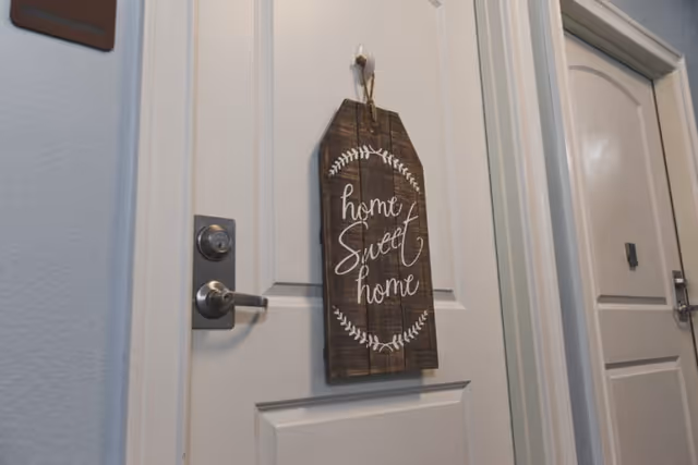 White interior door in a hallway with a wooden 'home sweet home' sign hanging on it and a silver handle.