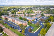 Aerial view of Park At Franklin senior living facility showing multiple large brick buildings surrounded by trees, parking lots, and roads under a partly cloudy sky.