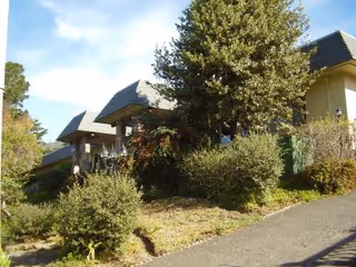 Exterior of The Chalet Montara showing the entrance with surrounding shrubs and trees.