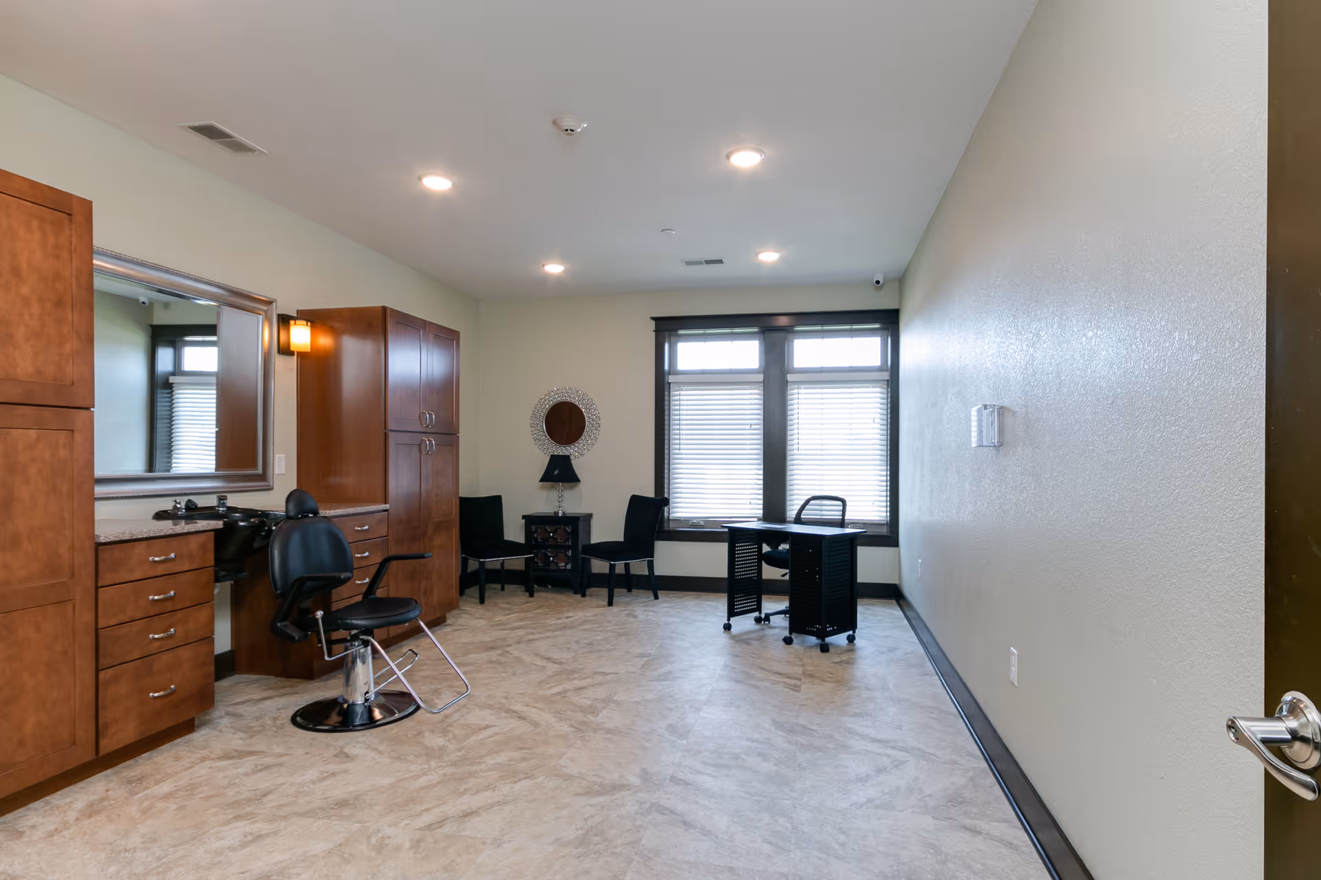 Interior room featuring a salon chair and wooden cabinetry on the left with seating and a small desk by windows at the far end.