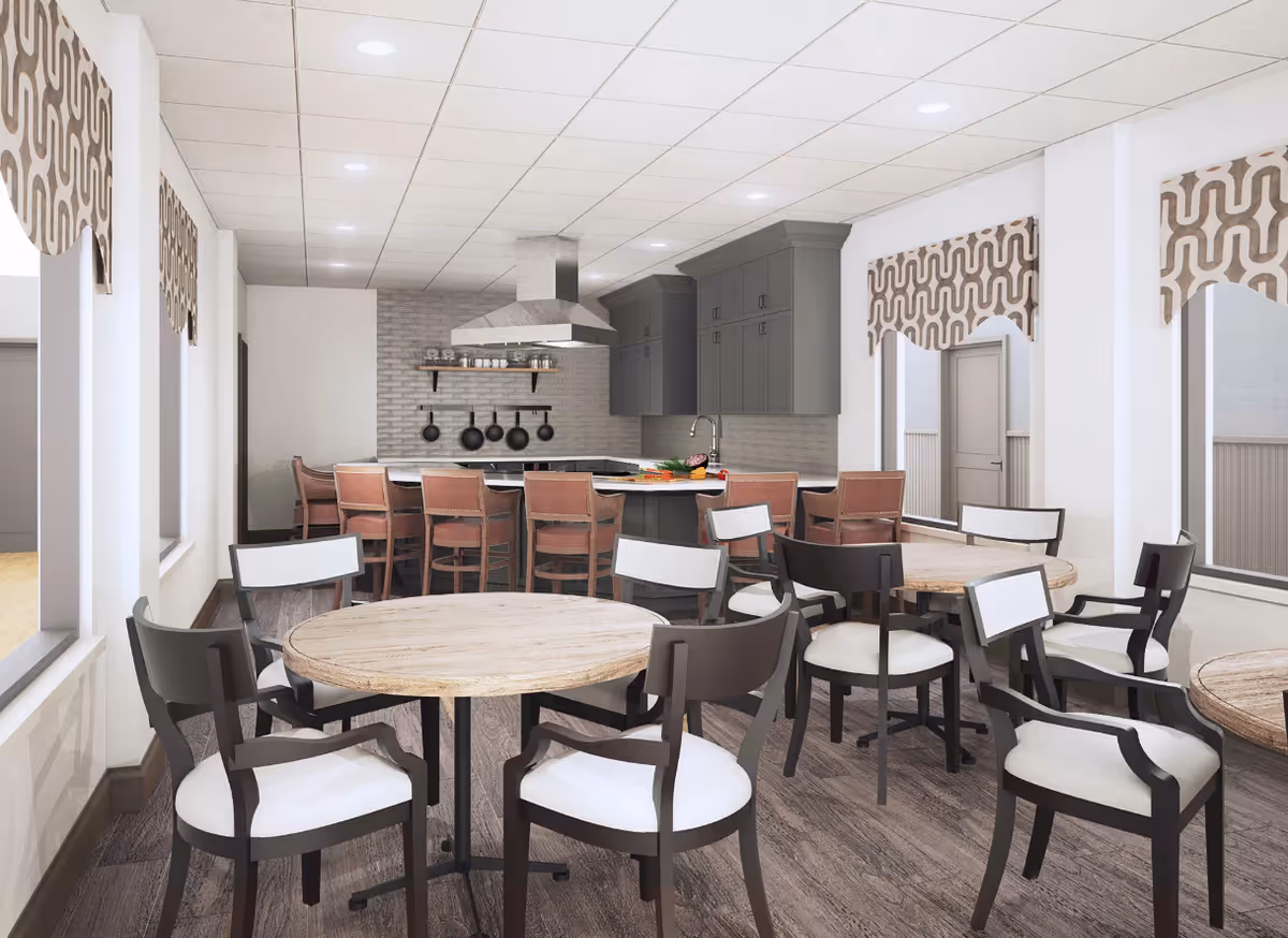 Communal dining area with round wooden tables and chairs facing an open kitchen island with barstools and grey cabinetry.