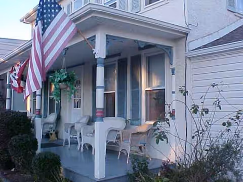 Front porch of a senior living facility with white chairs and an American flag.