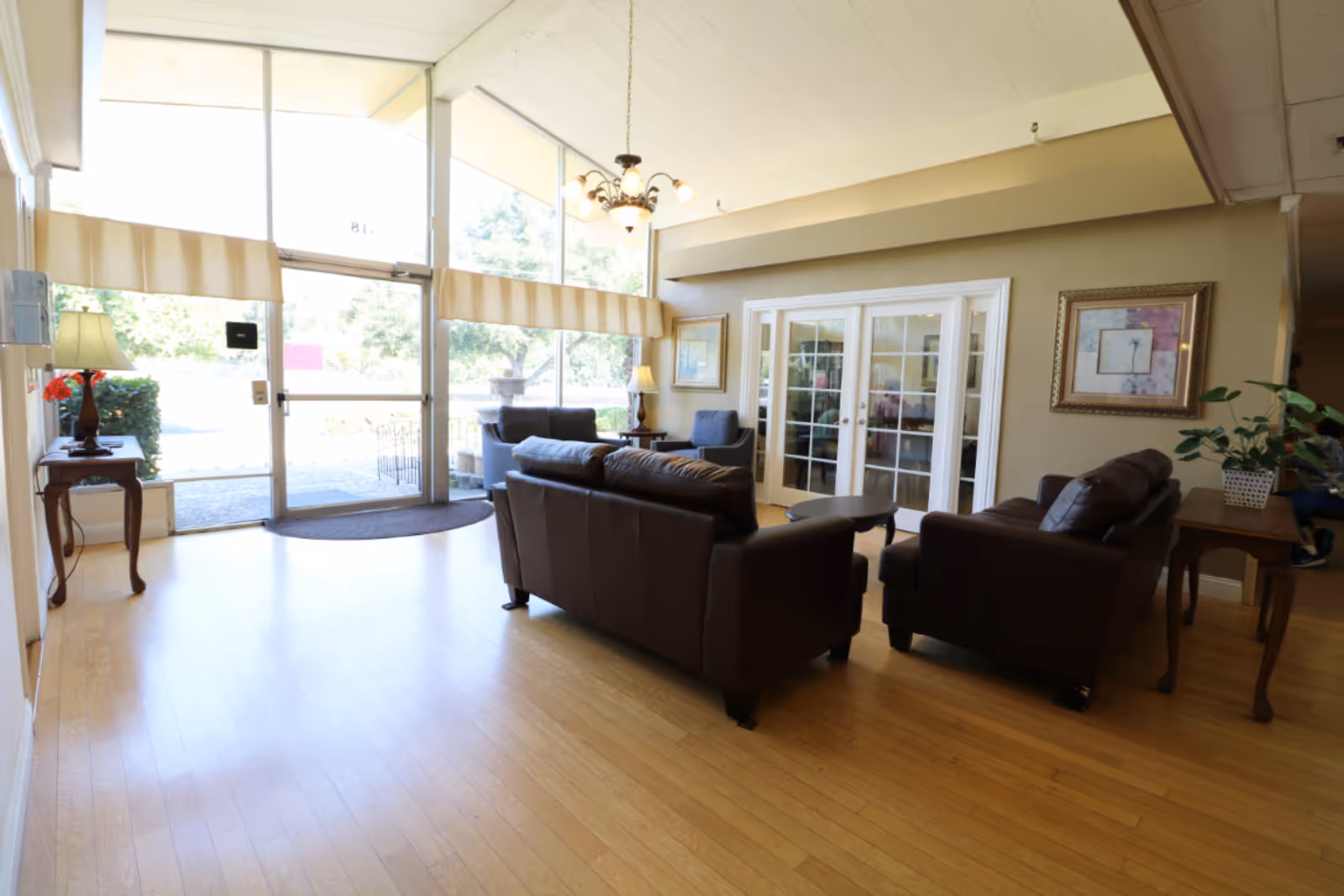 Bright senior living facility lobby with leather sofas, armchairs, glass entrance doors and wooden floors.