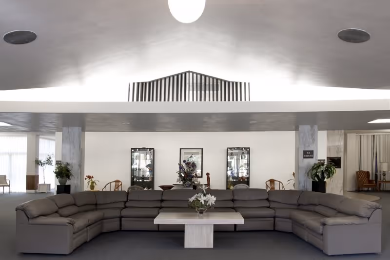 A spacious interior lounge with a large curved gray sectional sofa, coffee table and display cabinets against a white wall.