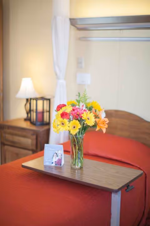 A cozy senior care bedroom with a vase of flowers on a small bedside tray.