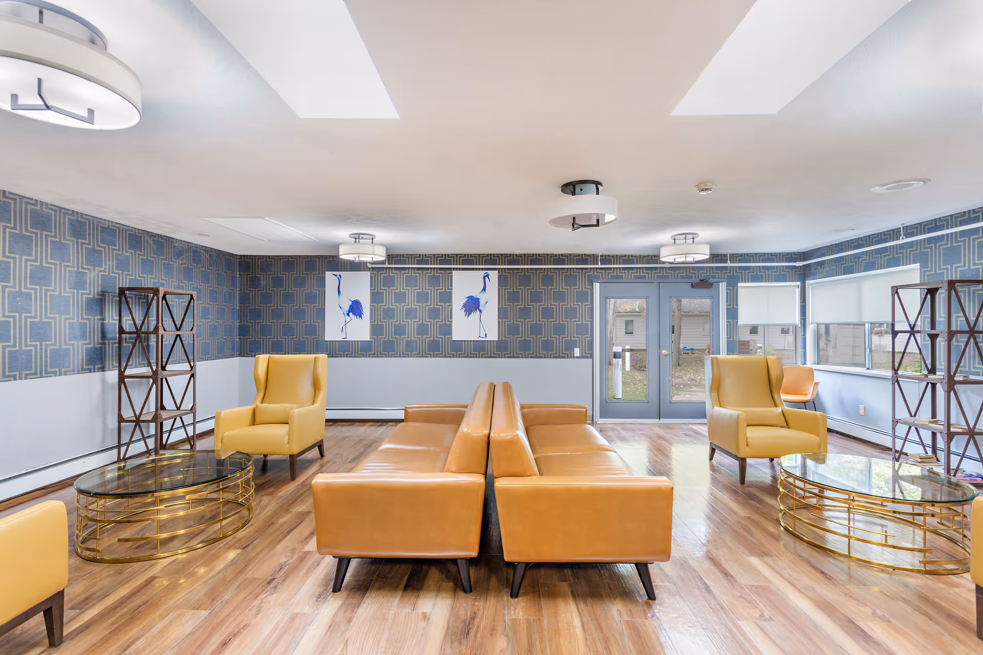 Spacious common lounge with tan leather sofas and yellow armchairs arranged around glass-and-gold coffee tables in a patterned interior.
