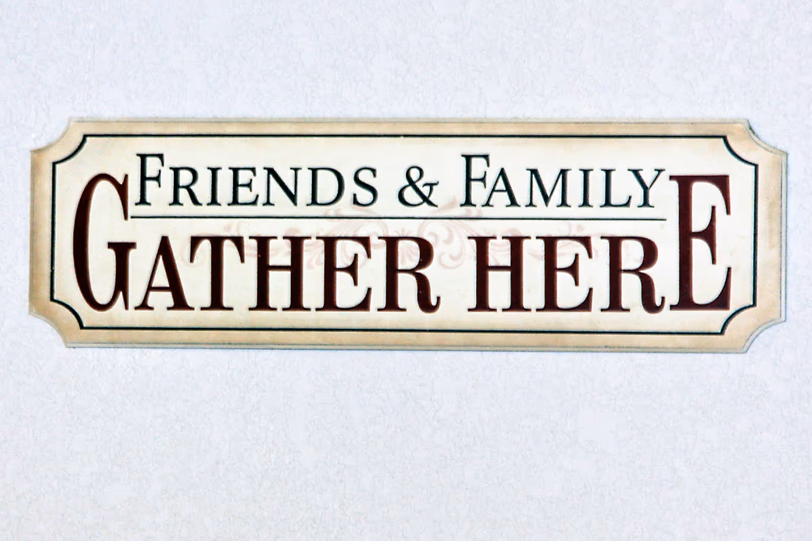 A decorative sign on a wall with the text 'Friends & Family Gather Here' in large, bold letters.