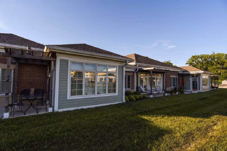 Exterior view of a single-story senior living facility with large windows, patios, and a grassy lawn.