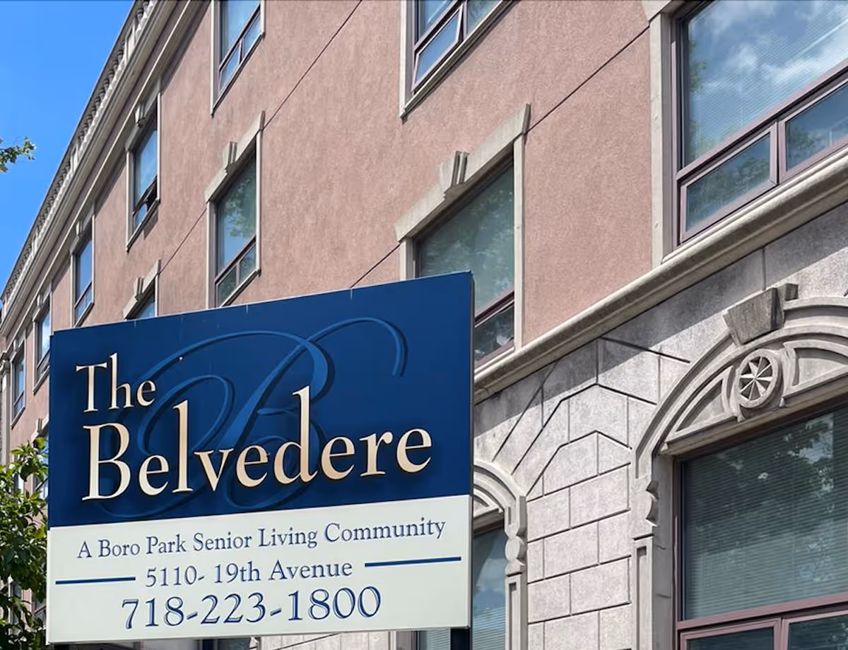 Blue and white sign reading "The Belvedere" mounted on the facade of a multi-story senior living building with windows.
