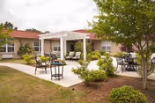 Outdoor courtyard with patio seating, a pergola, and landscaped shrubs in front of a single-story building.