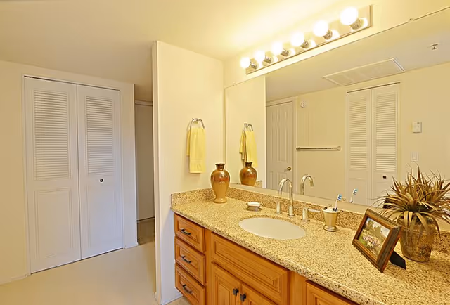 Bright bathroom with a granite-topped wooden vanity, sink, large mirror, and decorative items.