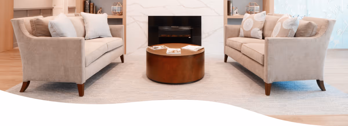 Two beige sofas facing each other around a round wooden coffee table in a cozy living room with a fireplace.