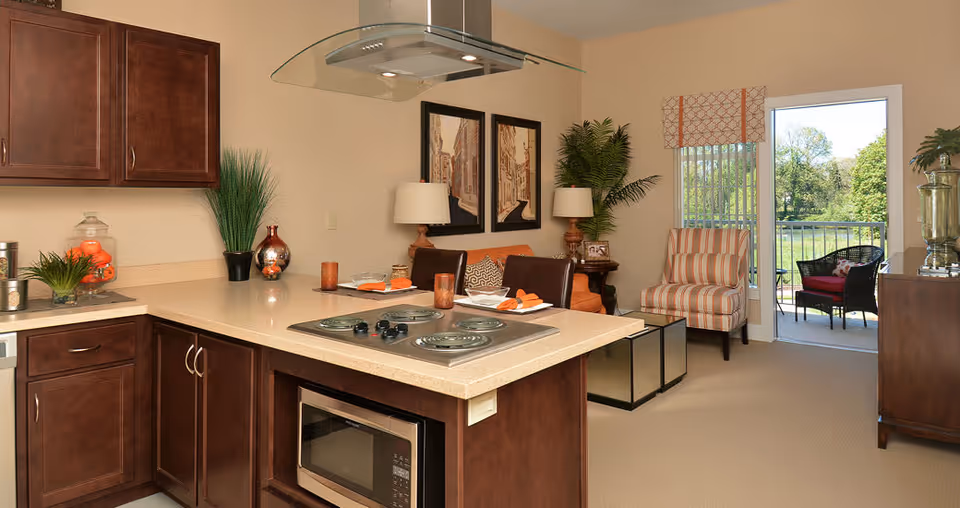 Open-concept kitchen with a central island and stovetop opening to a furnished living area and balcony.