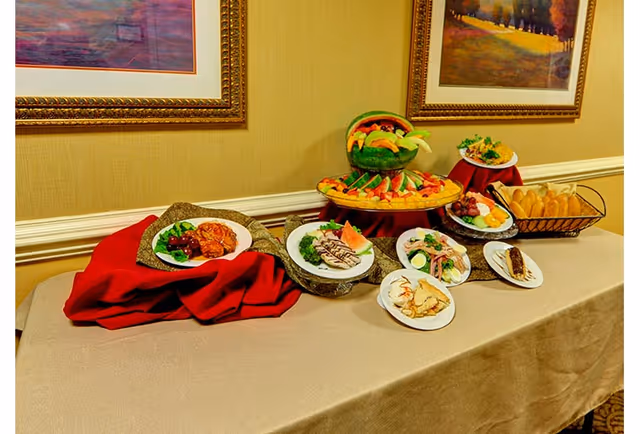 Buffet table in a dining area displaying plated appetizers, breads, and a tiered fruit centerpiece beneath framed wall art.