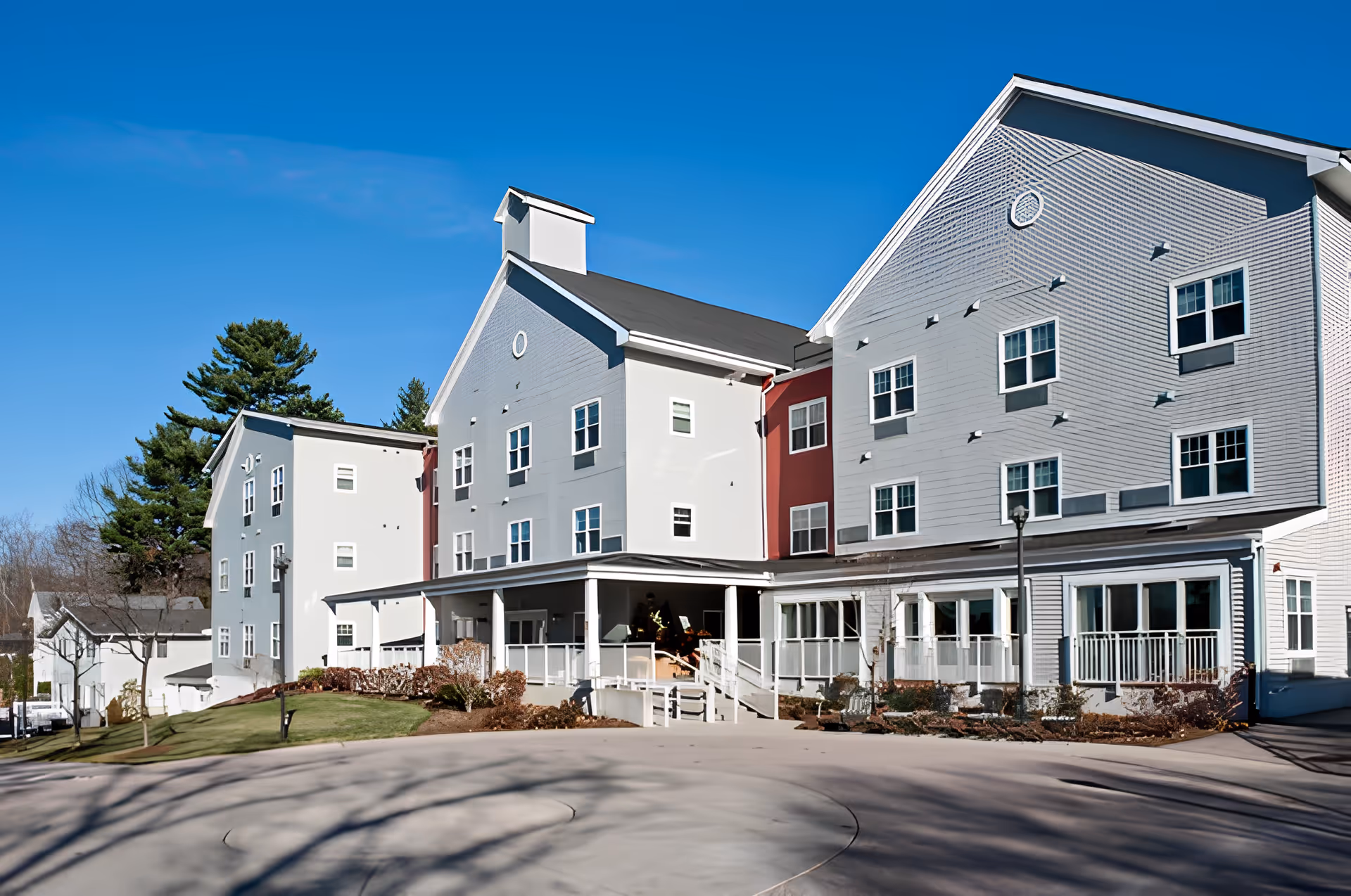 Front exterior of a multi-story senior living residence with a covered entrance, porches, and many windows under a clear blue sky.