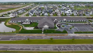 Aerial view of Boden Senior Living facility showing a large central building with a dark roof surrounded by multiple smaller residential buildings. The facility is bordered by roads and has landscaped green areas and a small pond.