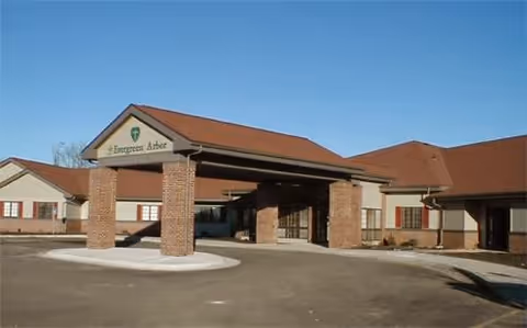 Front entrance of a single-story brick and stucco retirement building with a covered porte-cochère and clear blue sky.