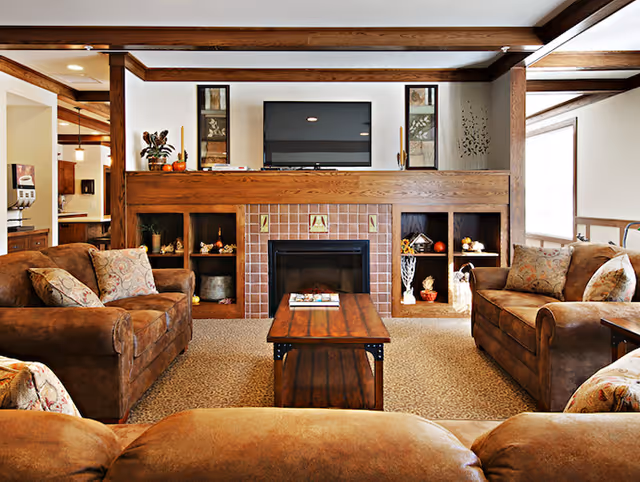 Cozy living room with brown leather sofas arranged around a wooden coffee table and a fireplace with built-in shelving and a wall-mounted TV.