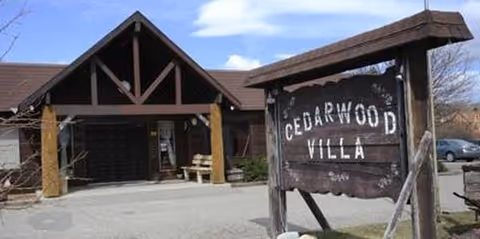 Exterior view of Cedar Wood Villa entrance with rustic wooden sign in foreground.