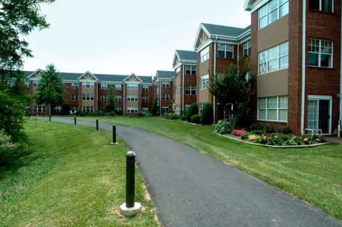 Curved paved walkway and manicured lawn lead to brick senior living buildings.