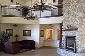 Spacious interior common room featuring a stone fireplace, seating area, chandeliers, and an upstairs balcony.