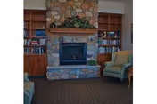 Interior common room featuring a stone fireplace centered between built-in bookshelves with armchairs nearby.