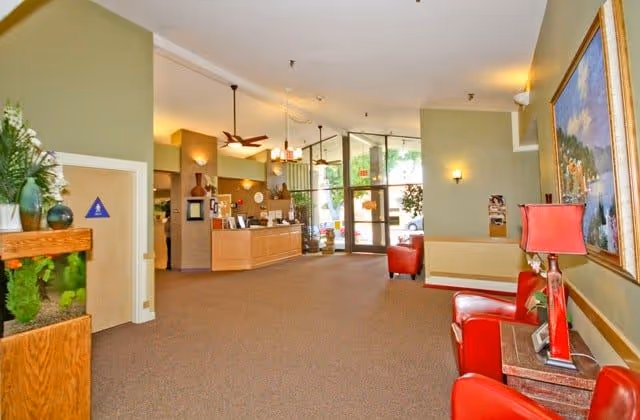 Spacious lobby of a senior living facility featuring a reception desk, red chairs, an aquarium, and glass entrance doors.
