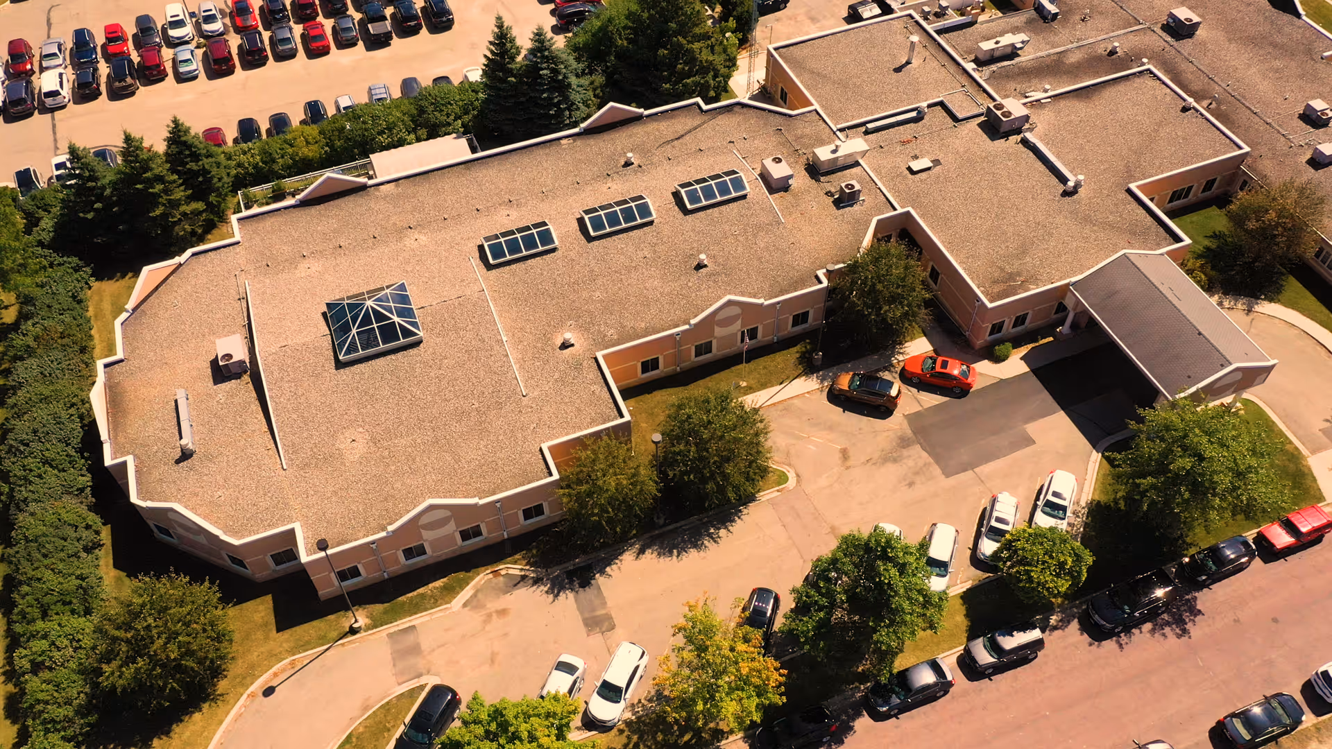 Aerial view of Oaklawn Rehabilitation Center showing the building with a flat roof, multiple skylights, surrounded by trees and parking lots filled with cars.