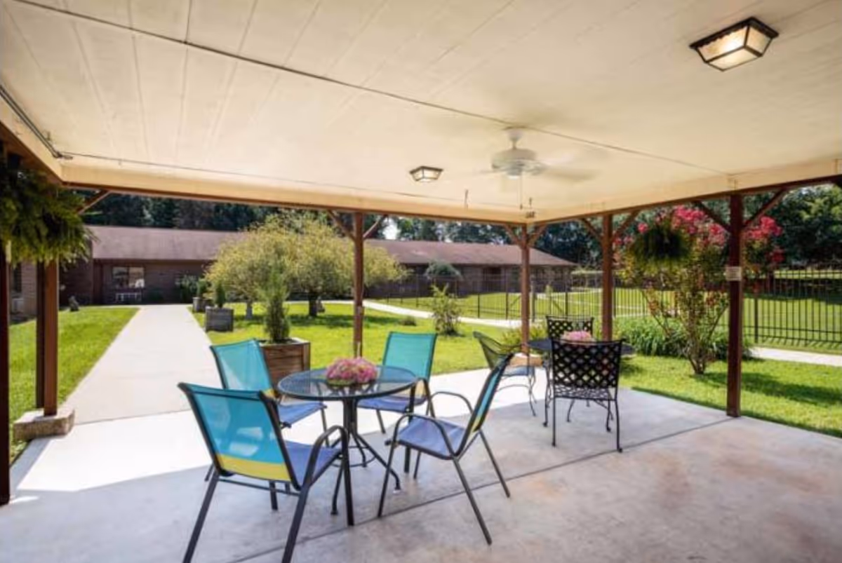 Covered outdoor patio with metal chairs and a table overlooking a grassy yard.