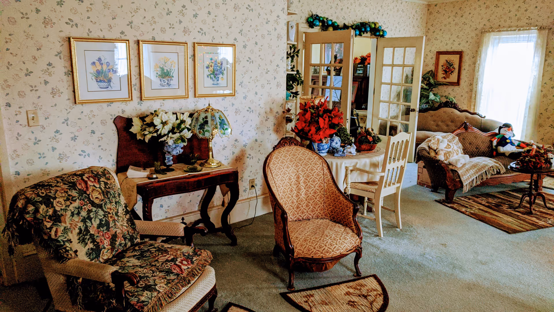 Warmly decorated living room with floral wallpaper, upholstered chairs, a sofa, and side tables.