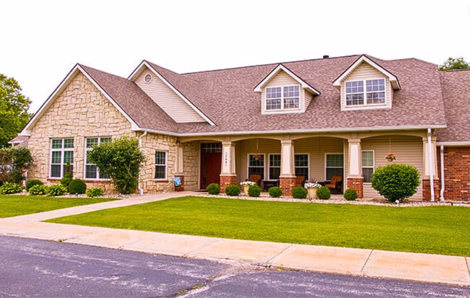 Exterior view of a single-story building with a stone and siding facade, multiple windows, a covered porch with columns, and a well-maintained lawn in front.