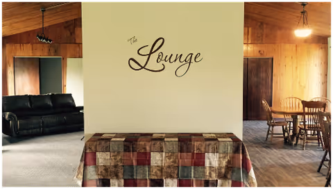 Interior common lounge area with a central wall labeled "The Lounge", a covered table in front, a leather sofa to the left and a dining table with chairs to the right.