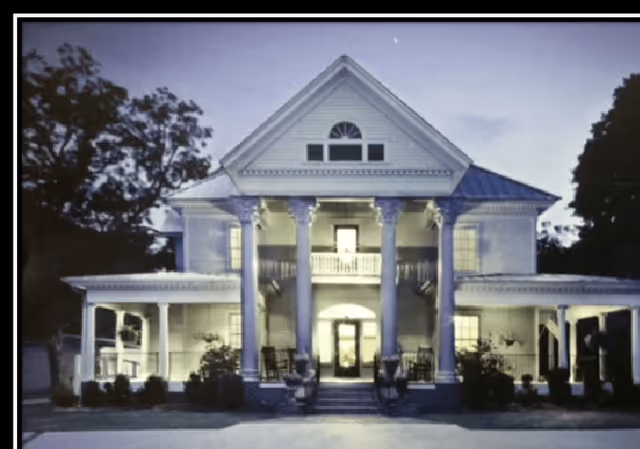 Front exterior of a large two-story historic-style house with a columned porch lit at dusk.