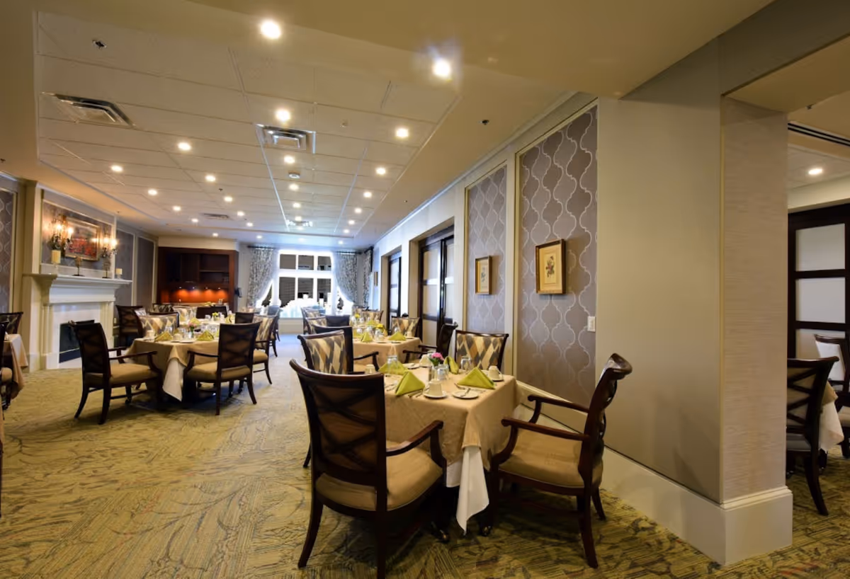 Spacious dining room with multiple set tables and chairs, decorative wallpaper, and a fireplace.