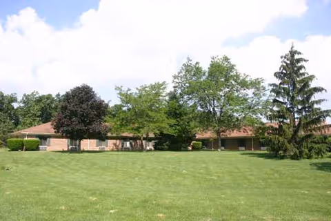 Single-story brick facility with red roof and expansive green lawn and trees.