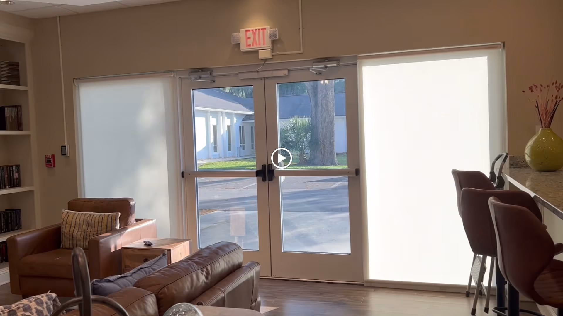 Bright senior living common room with leather sofas, armchairs and bar stools facing double glass exit doors.