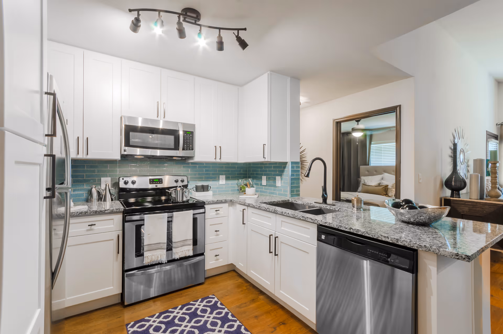 Modern kitchen with white cabinets, stainless steel appliances, granite countertops and a teal subway tile backsplash.