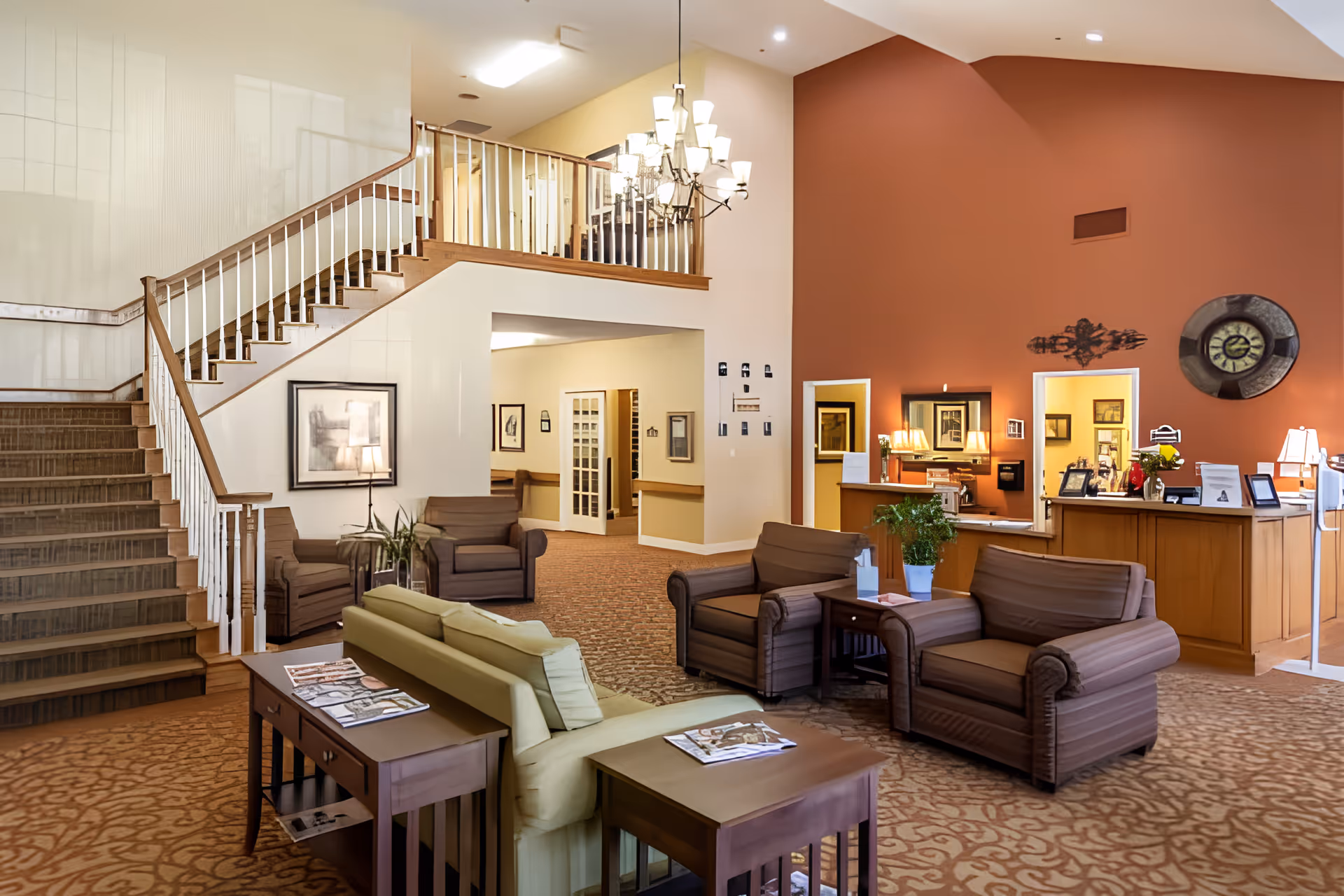 Spacious senior living lobby with seating area, a reception desk, and a staircase to an upper level.
