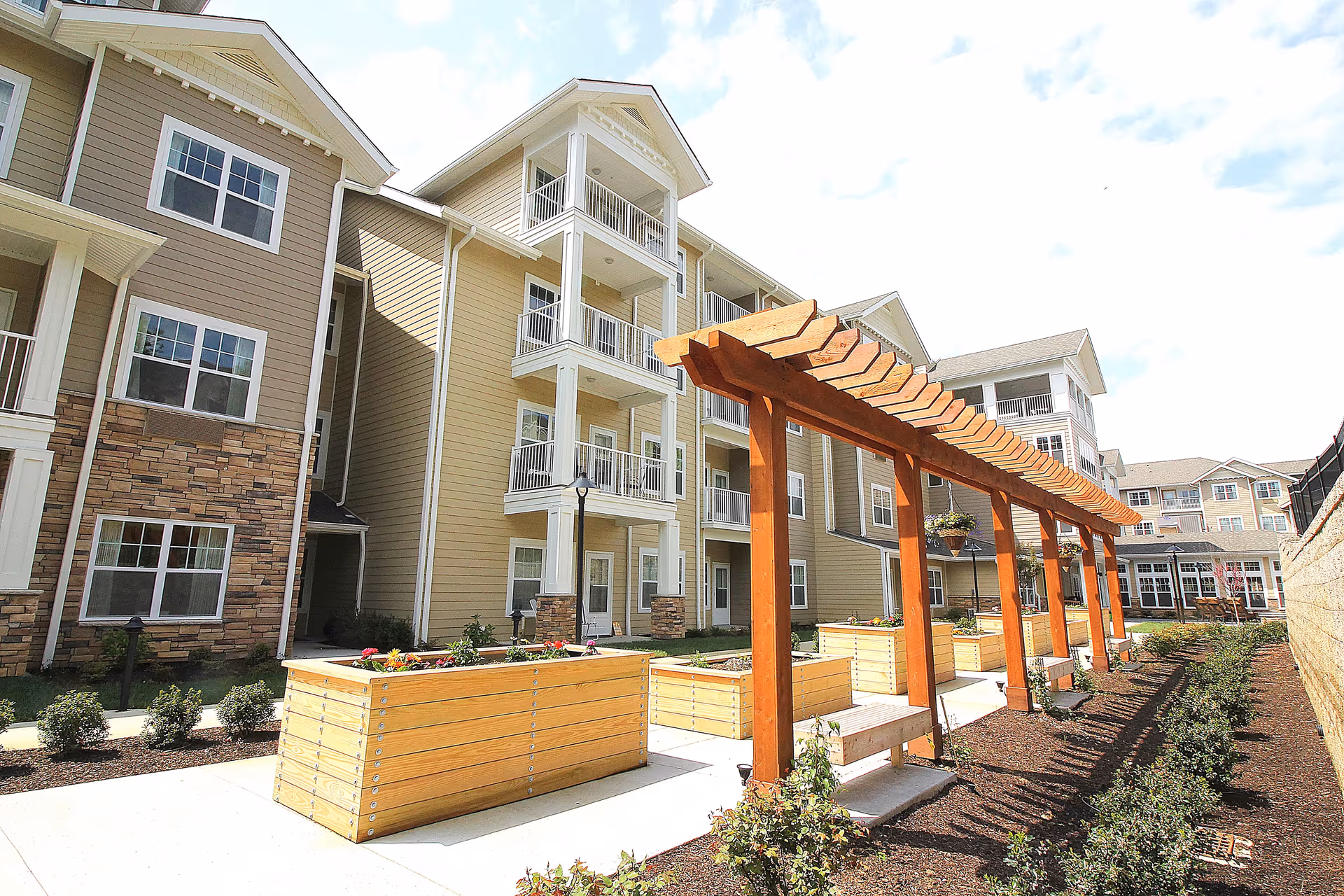 Courtyard of a multi-story senior living building with a wooden pergola, raised planter boxes, and balconies.