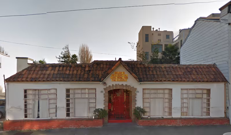 Front exterior view of Belen's Residential Care Home, a single-story building with a red tiled roof, white walls, and large windows with curtains. The entrance has a red decorative gate and a sign above it that reads 'Belen's Residential Care Home for the Elderly'.